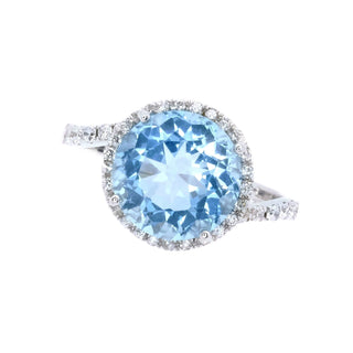 A silver-toned halo ring featuring a large round light blue topaz center stone and small clear accent stones along the halo and band, shown on a plain white background.